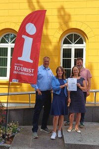 Bild vergr&ouml;&szlig;ern: B&uuml;rgermeister Eckhard Graf (vl.), Uta Steffen (Projektleitung Herzogtum barrierefrei bei der HLMS), Jaana Trebesius (Leitung Tourismus und Stadtmarketing Ratzeburg) sowie G&uuml;nter Schmidt (Gesch&auml;ftsf&uuml;hrer der HLMS), bei der &Uuml;bergabe der Urkunde &raquo;Reisen f&uuml;r Alle&laquo; vor der Tourist-Information Ratzeburg.